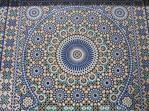 Lots of trapezoids, triangles, and arrow shapes placed in circled such that the gaps look like stars. Overall shape looks like a circle with circles around it, and then there is a rectangular border at sides also decorated with similar shapes.