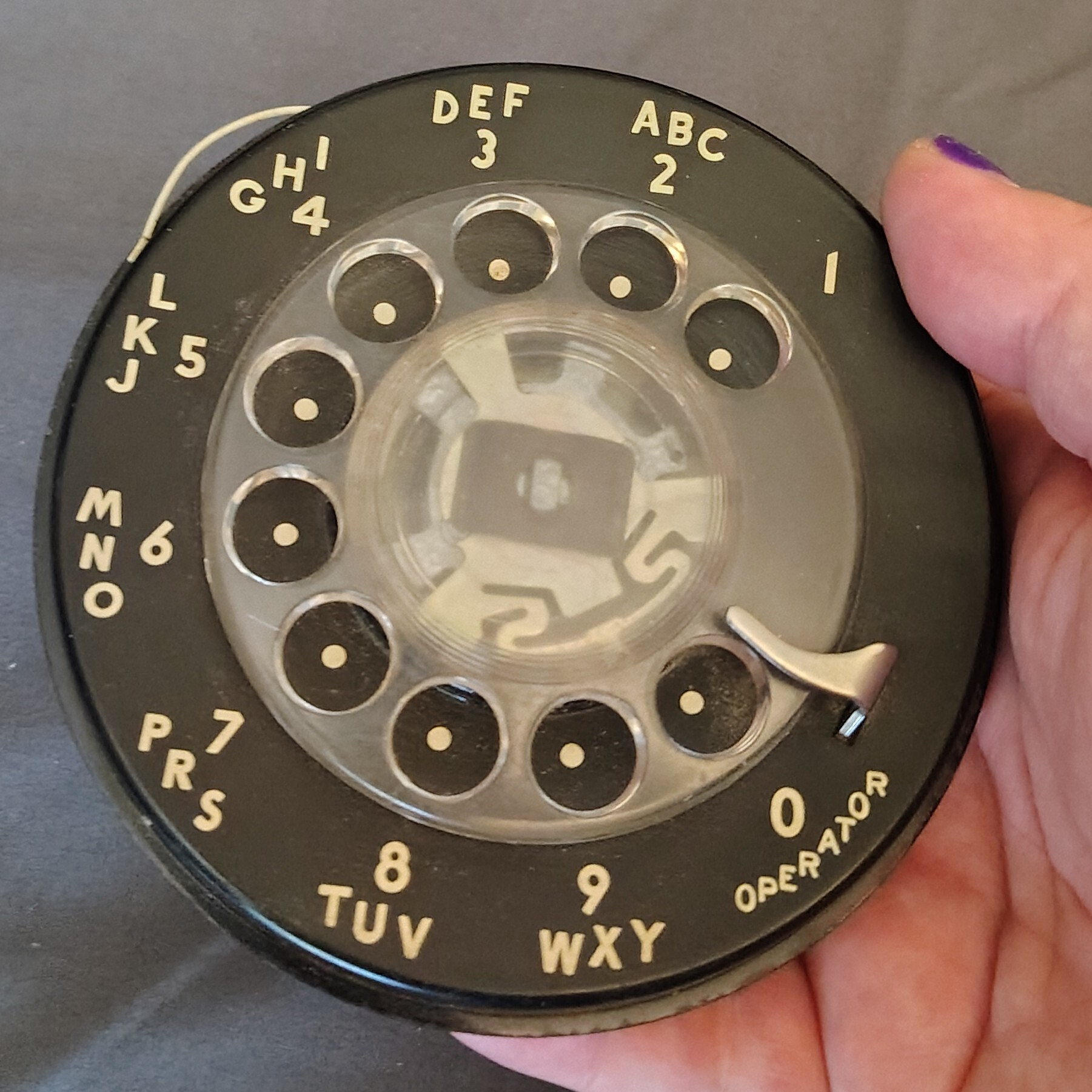 Photo of a rotary phone dial held in my hand.