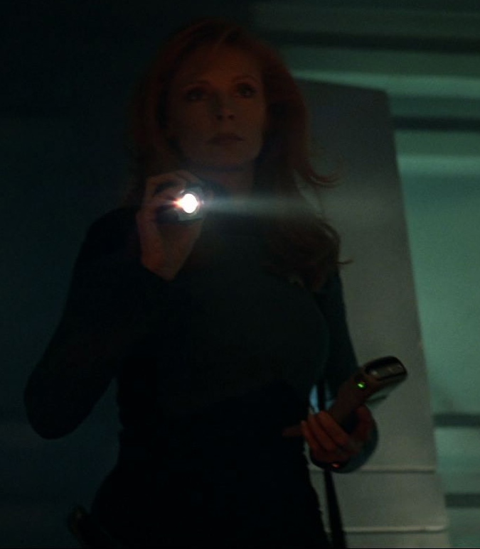 Dr. Crusher holding a small palm-sized flashlight, her arm in an aloft yet scrunched "please give me a muscle cramp" position.