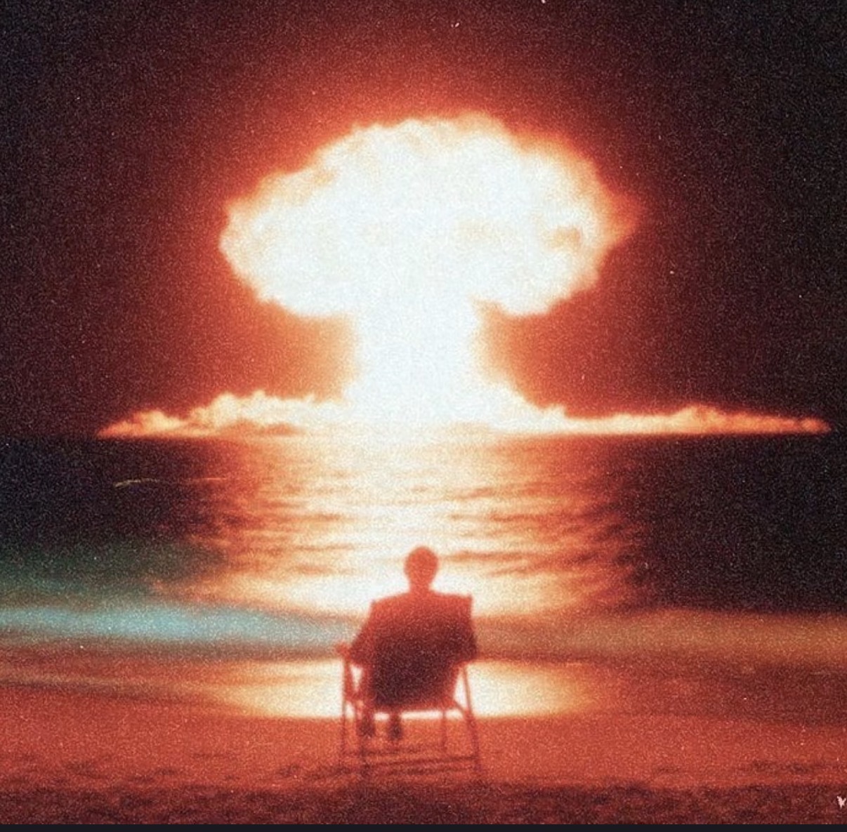 a silhouette of a person sitting in a lawn chair while watching a nuclear explosion off in the distance