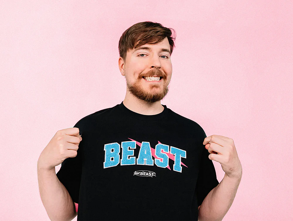 Image of MrBeast, situated against a white background, smiling and wearing a "BEAST" graphic tee